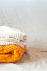 Handmade orange and white chunky knit sweaters lie against a background of textured linen. High quality photo