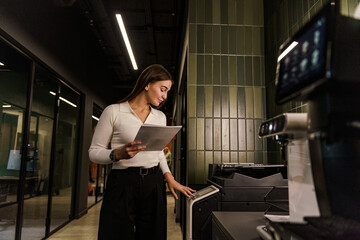 A woman in a jacket is printing on a printer, an employee in a specialist copywriter company. A...