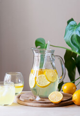 Fresh homemade lemonade in glass jug and glasses on the wooden board and table with tropic plant. Vertical shot