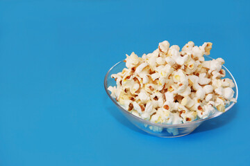 White delicious fried airy popcorn in a transparent plate on a blue background