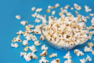 White delicious fried airy popcorn in a transparent plate on a blue background