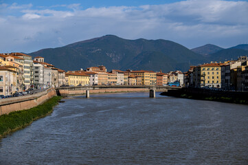 View of old town of Pisa on the river Arno with mountains in background