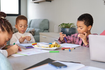 Three children having a snack while painting or doing the homework at home.