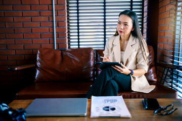 Portrait of cheerful Asian businesswoman professional in black business suit using a digital tablet...