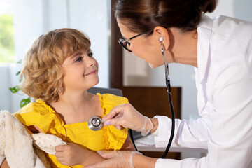 Female doctor checking child's lungs during medical checkup in medical exam room at the clinic....