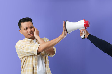 Photo of a young Asian man feeling disturbed at work when his secretary shouting with a megaphone.