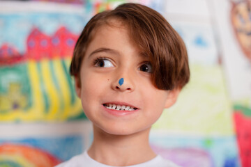 Obraz premium Child painting displaying his artwork on the wall. watercolor and paint on his face nose 
