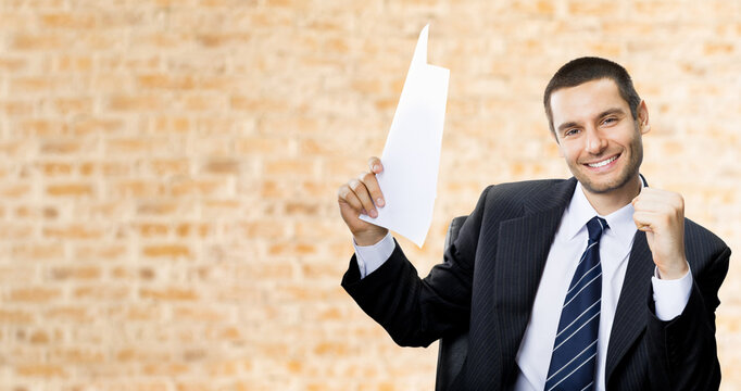 Happy smiling successful gesturing business man with document at office brown bricks wall background.