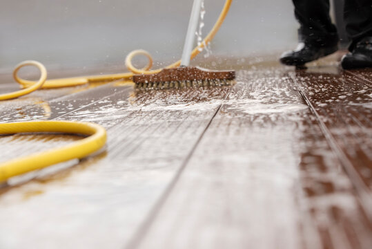 Blurred detail of a man with a scrubbing brush during spring cleaning of a wooden terrace floor with sparkling water .