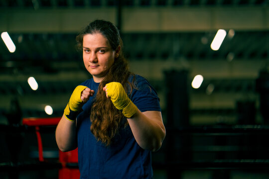portrait focused Boxer girl in yellow boxing bandages standing in a boxing stance on a dark background in a gym before a fight