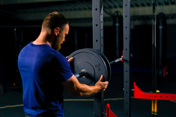 male athlete trainer adds weight to the barbell in the gym increases the load on the body of the...