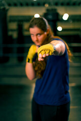 portrait focused Boxer girl in yellow boxing bandages standing in a boxing stance on a dark...