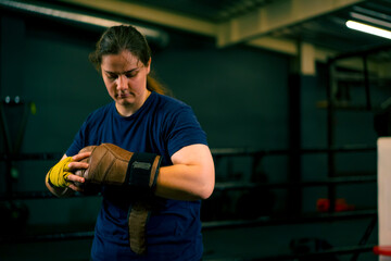 girl boxer puts on brown boxing gloves over bandages before starting sports training in the ring