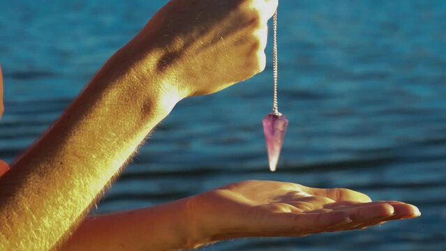 Women's hands holding a pendulum with a lake in the background