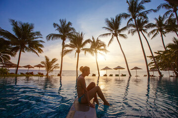 spa, silhouette of woman relaxing near swimming pool on the beach at sunset in luxury hotel - obrazy, fototapety, plakaty