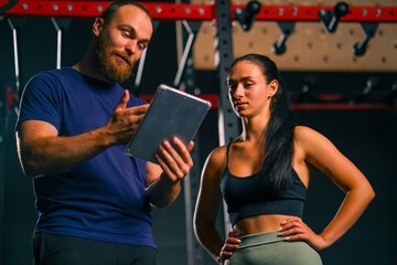 a male trainer holds a tablet in his hands and shows a training schedule to a female athlete...