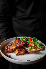 chef or waiter hold plate of grilled pork ribs with baked eggplant 