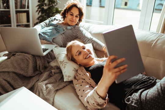 Young lesbian couple using electronics together on the couch at home