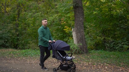 Fototapeta na wymiar A young father walks through the forest with a sleeping child in a stroller. A man walks in an autumn park.