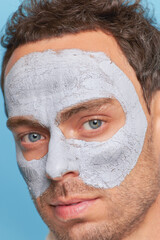 Portrait of serious model guy with grey eyes and clay facial mask, cosmetic treatments for men, male skincare concept, copy space