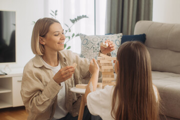 Obraz na płótnie Canvas Family plays board game. Cheerful and friendly young woman and her daughter are having fun playing Jenga together. Family spending time together at home on day off.