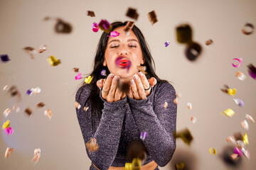 Cheerful beautiful brunette girl blowing confetti from her hands. Celebration of the holiday. Festive New Year's atmosphere. Fun event. Christmas concept.