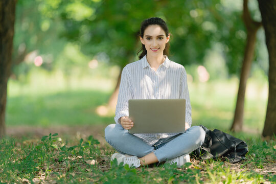 Smiling young Woman laughing at her laptop computer in the park. Women studying in an outdoor, working on computer or video meeting.