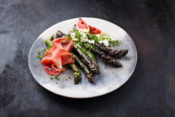 Traditionell glasierter lila Spargel mit Prosciutto Schinken, Feta Käse und Feigen serviert als Nahaufnahme auf einem Design Teller mit Textfreiraum