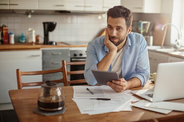 Young man using a tablet while going over financials in the kitchen