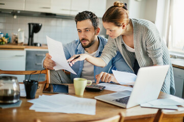 Young couple going over bills and payments together in the kitchen - obrazy, fototapety, plakaty