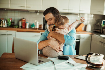 Young father embracing his daughter while paying bills in the kitchen