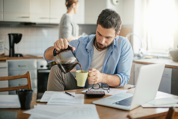Young man drinking coffee while going over bills and payments in the kitchen