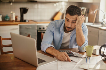 Stressed young man going over bills and payments in the kitchen