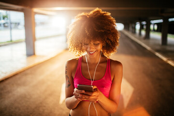 Young fit woman using a smartphone before jogging under a bridge in the city