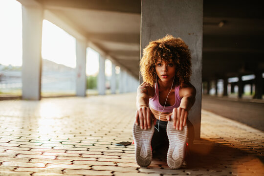 Young fit woman stretching before jogging under a bridge in the city