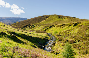 Beautiful Scottish landscape with mountains and a river creek. Amazing wild nature on a sunny day. Shot taken on a trip around North Coast 500