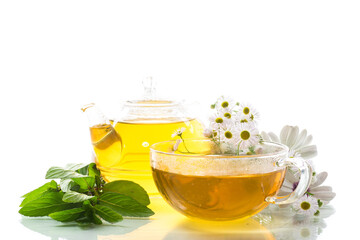 Chamomile flower tea in glass cup and teapot, on white background.