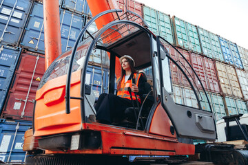 Caucasian woman in cabin wearing hard hat working as operator of loader crane machine in shipping...