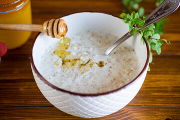 milk oatmeal porridge with honey for breakfast in a bowl wooden table.