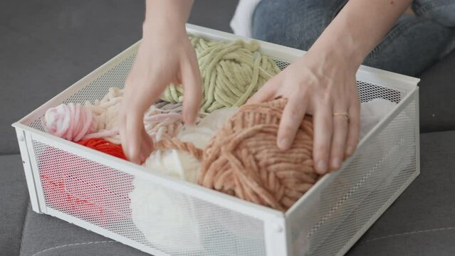 A woman puts a drawer of yarn in front of her for future arigurumi knitting at home on the couch. Relaxation and rest at home.