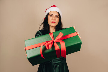 Studio shot of beautiful happy joyful excited girl in santa hat and green dress holding gift box in hand. Merry Christmas. New year concept.
