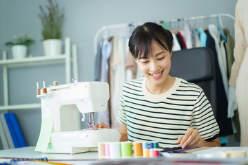 Happy beautiful Asian young woman working in the fashion design studio, professional female fashion...
