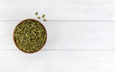 Peeled pumpkin seeds in a wooden bowl on a white background. Top view. Copy space.