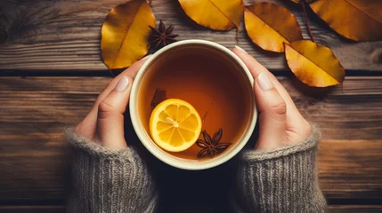 Fotobehang Woman holding a cup of hot tea with lemon, leaves on wooden autumn background. Hot drink concept. © Zahid