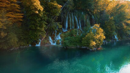 Waterfall flowing in autumn forest at national park during warm sunset light. Cascade in woods with colorful trees and fresh water.