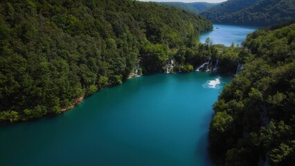 Turquoise water of lake in mountain forest with pine trees. Aerial view of blue reservoir and green woodland in summer.
