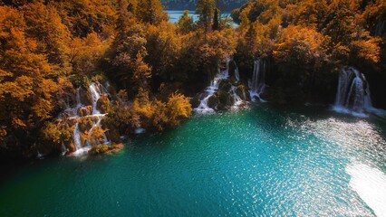 Yellow foliage on trees in autumn mountain forest with lake. Clear water of waterfalls. Emerald green reservoir. Sunny weather and bright day.