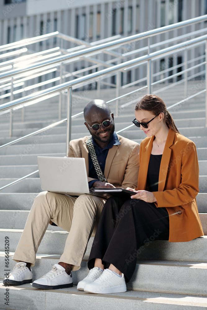 Poster confident african american male employee explaining data to female colleague and pointing at paper d