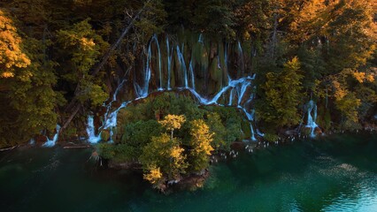 Emerald water in a mountain forest lake with bright autumn trees. Aerial view of waterfall in golden woods. Clear aqua in reservoir.