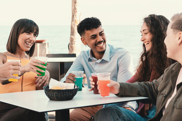 Fototapeta premium Friends Chatting on Beachfront Terrace - A diverse group of young adults converse, including an African-American and a girl with vibrant short hair, bonding over stories and laughter.